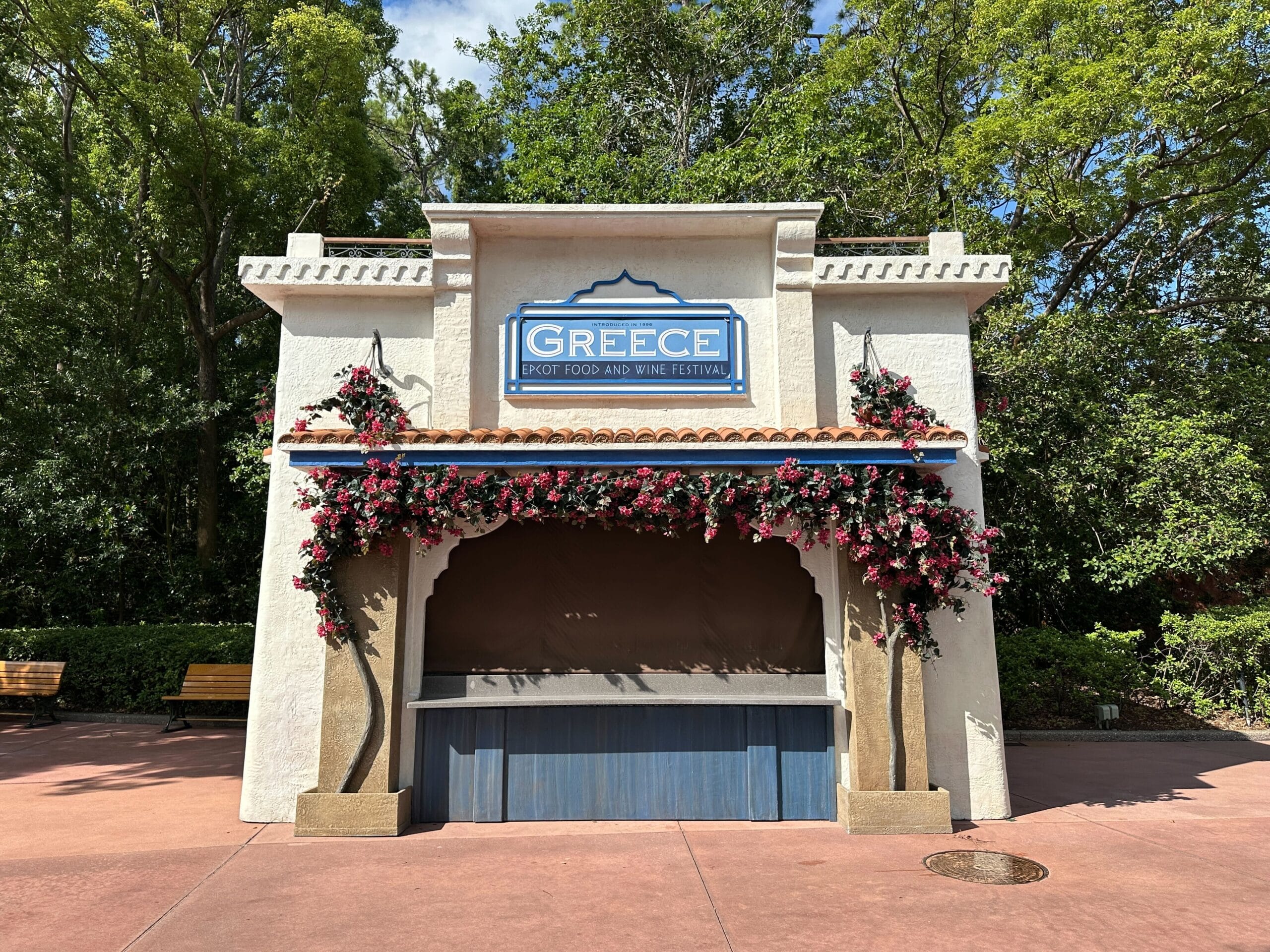 A closed Greece food booth in preparation for the 2025 EPCOT International Food & Wine Festival, adorned with flowers.